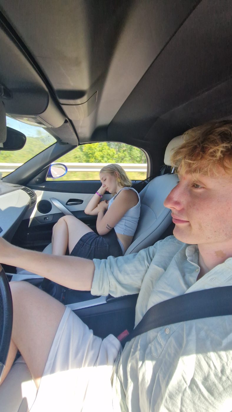 Lui au volant, elle endormie contre la vitre côté passager, autoroute bordée d'arbres.