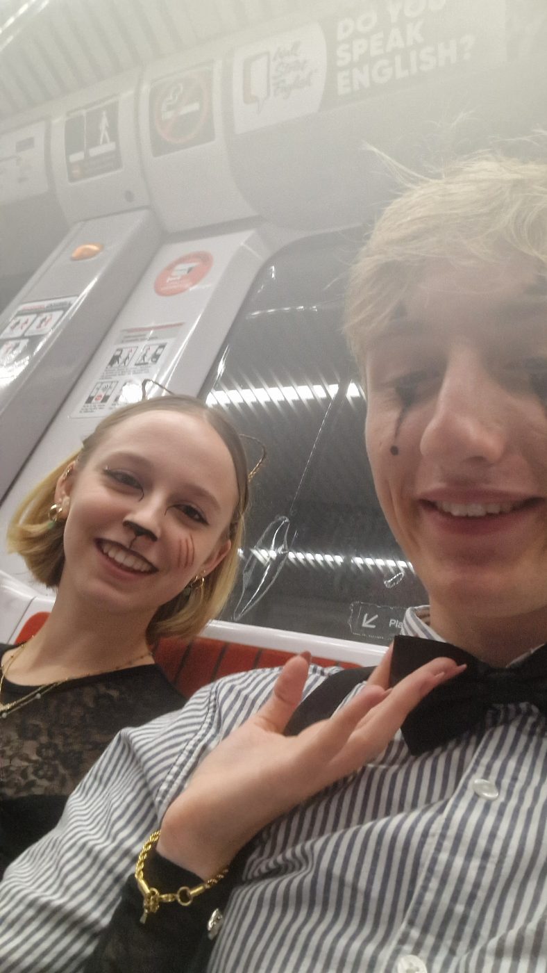 Selfie dans un tram le soir : elle a des moustaches de chat dessinées, lui une larme peinte et un nœud papillon.