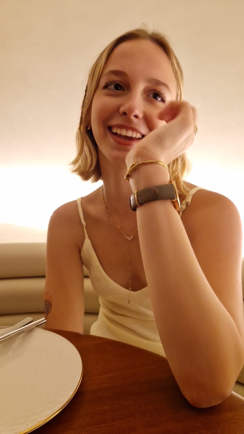 Elle attablée dans une lumière très chaude, la joue posée sur le poing, en train de rire en regardant sur le côté.