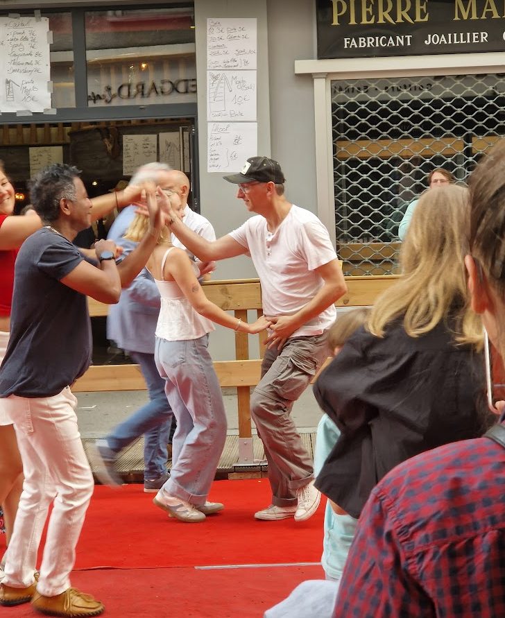 Des gens dansent sur un tapis rouge dans la rue ; elle danse au centre, en haut blanc et jean.