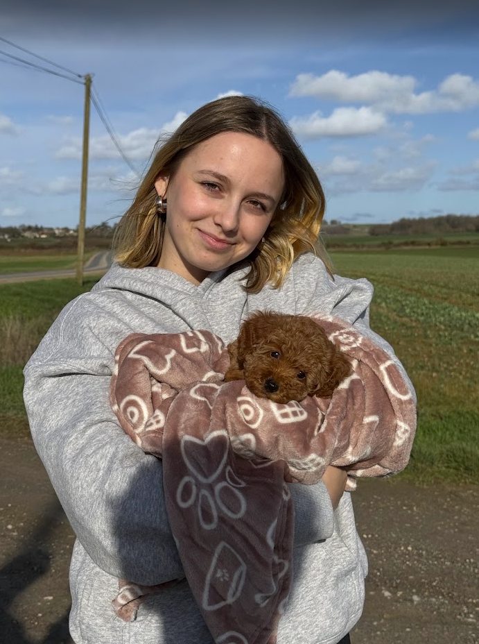 Au bord d'une route de campagne, elle tient dans ses bras un tout petit chiot roux emmailloté dans une couverture.